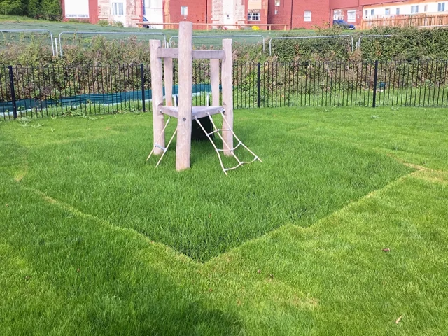 Grass mats with grass grown through underneath small wooden playground climbing equipment