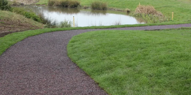 A golf pathway using our multi-coloured Jungle Mulch Rubber Mulch surface cover in a golf course, surrounded by grass and next to a pond