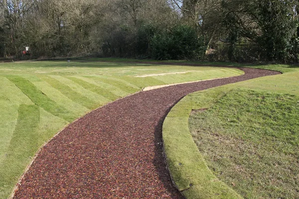 Striped artificial grass and red JungleMulch pathway in golf course