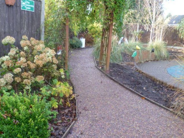 Playground rubber mulch path with green vegetation and wooden trellis arch