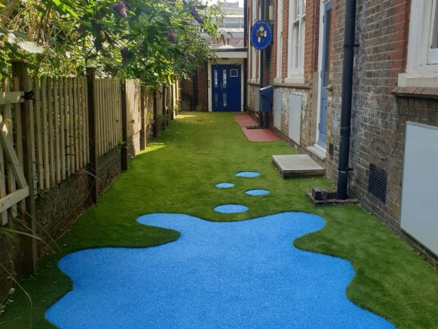 Artificial grass installed along a building with puddle shaped EPDM wear pad