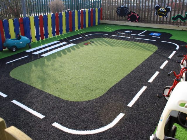 Artificial Grass used in a rectangular road track on a play area, with green artificial grass at the centre and black and white patterned artificial grass used for the road design.