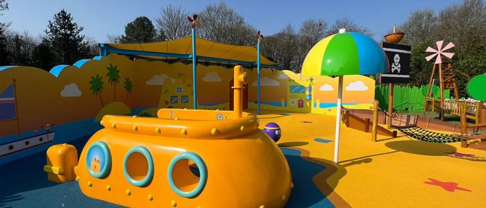 Yellow, orange, and dark blue coloured RubbaSmart wet pour rubber surfacing used to create a beach and sea design on a children’s playground. Playground structures on this site include a yellow submarine, beach umbrella and pirate ship.