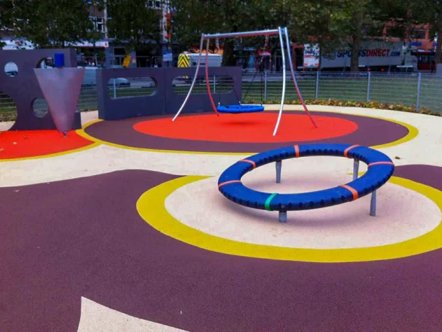 Wet Pour Rubber Playground with white base and purple, yellow, and red circle patterns around equipment