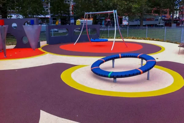 Wet Pour Rubber Playground with white base and purple, yellow, and red circle patterns around equipment