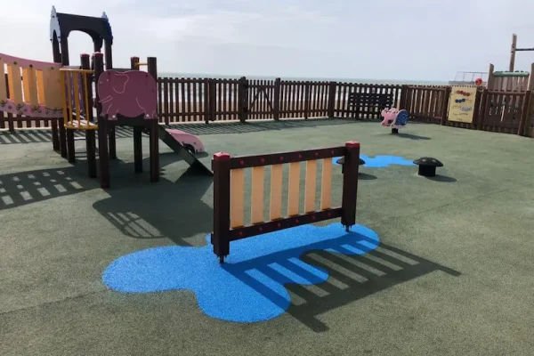 RubbaSmart wet pour rubber playground surfacing being used on a playground. Over green artificial surfacing, blue wet pour is used to create a puddle shaped design beneath some playground equipment