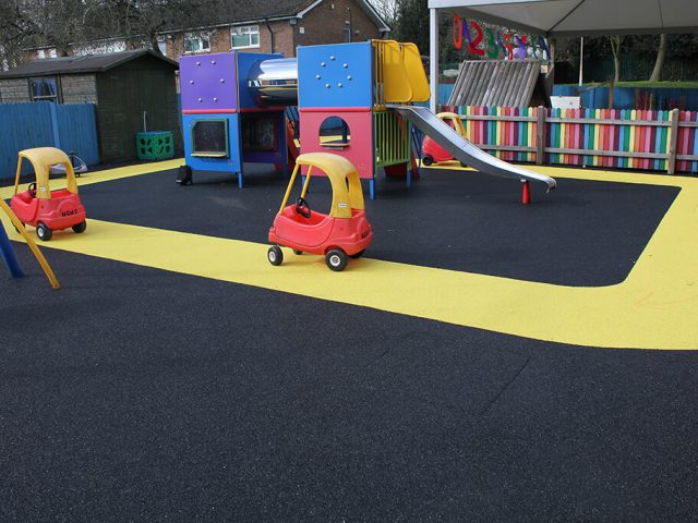 Vibrant yellow track around playground equipment with black safety surfacing. A racing track for children's car toys