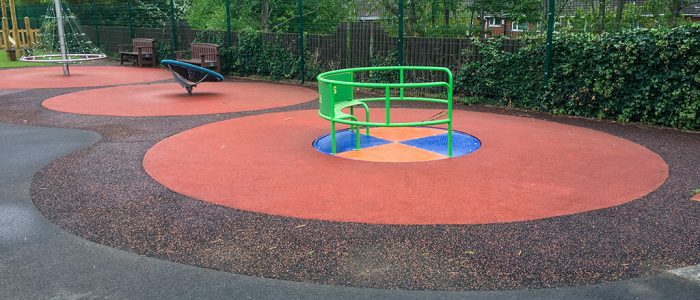 SmartPave playground installation with red mixed rubber surfaces around wheelchair accessible roundabout