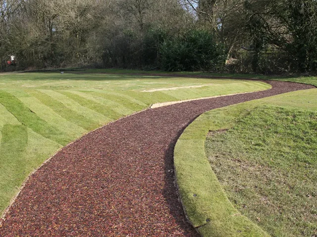 Striped artificial grass and red rubber mulch pathway in golf course